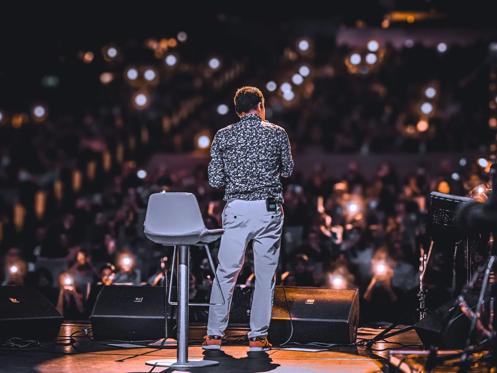 A speaker on an event stage facing a large audience